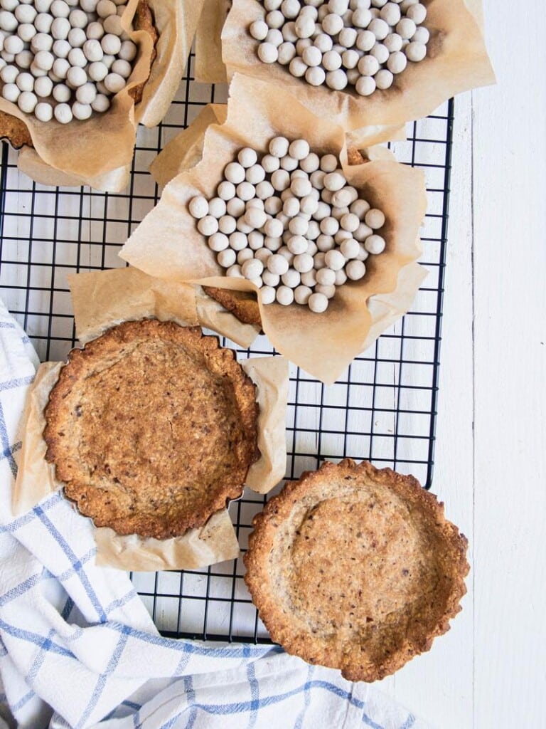 Small tart crusts filled with ceramic baking beads cooling on a cooling rack.