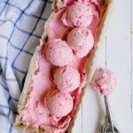 Five balls of cream cheese ice cream on a top of a loaf tin used as an ice cream container. Ice cream scoop on the right and blue-striped tea towel on the left.